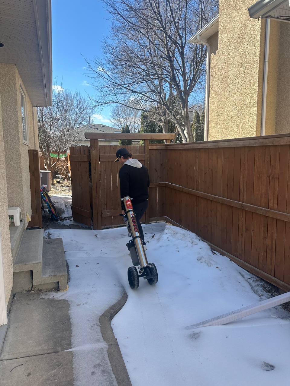 Worker moving a tall equipment tank on a hand truck beside a house